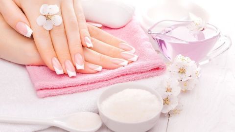Gepflegte Hände mit French Nails liegen auf einem pinken Handtuch; im Hintergrund sind Pflegeutensilien und Blüten sichtbar.