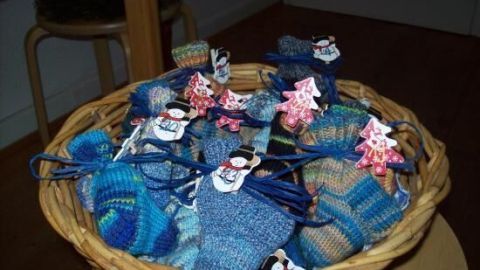 Ein Korb mit handgestrickten Babysocken in Blau- und Grüntönen, dekoriert mit kleinen Weihnachtsfiguren.