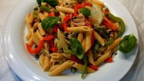 Penne sizilianisch liegt auf einem weißen Teller, garniert mit frischem Basilikum, Paprika und einer Zitronenscheibe.