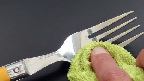 Mit Zitronensäure bekommt man strahlendes und glänzendes Besteck. Eine Gabel wird mit einem grünen Tuch gereinigt, um strahlendes Besteck durch Zitronensäure zu erreichen.