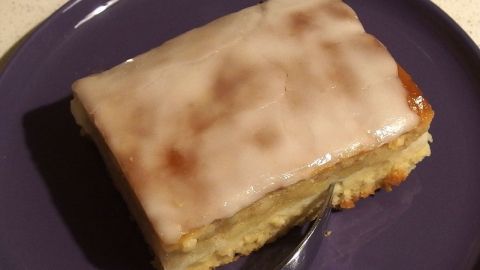 Aus Apfelsaft und Puderzucker einen Zuckerguss für Kuchen herstellen. Ein Stück Kuchen mit Zuckerguss aus Apfelsaft und Puderzucker liegt auf einem lila Teller in einer neutralen Umgebung.