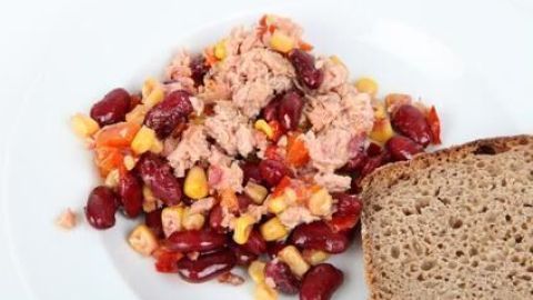 Thunfischsalat mit Bohnen, Mais und Paprika liegt auf einem Teller, begleitet von einer Scheibe Brot.