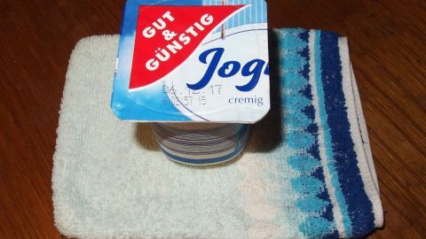 Ein Joghurtbecher steht auf einem kleinen Handtuch. Der Kontext ist eine einfache, saubere Oberfläche.