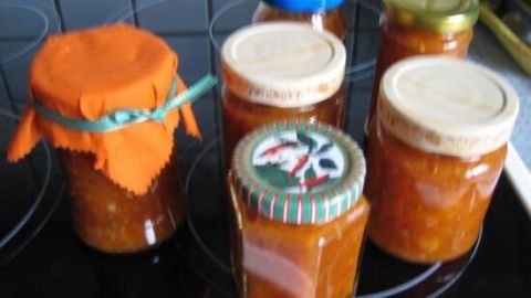 Gläser mit Aprikosenchutney stehen auf einem Herd; eines hat einen orangefarbenen Stoffdeckel mit Schleife.