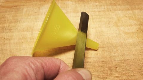 Eine gelbe Einfüllhilfe steht auf einem Holzbrett, während eine Hand einen Holzspatel hält, um Marmelade zu fördern.