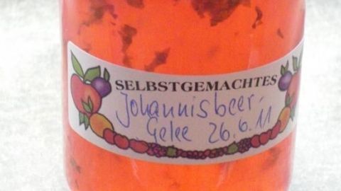Ein Glas mit selbstgemachtem Johannisbeer-Prosecco-Gelee steht auf einer dunklen Fläche und zeigt leuchtend rote Farben.