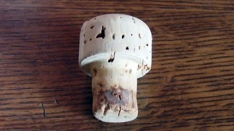 Ein Korken steht auf einem Holztisch und zeigt einige kleine Löcher, die durch die Benutzung entstanden sind.