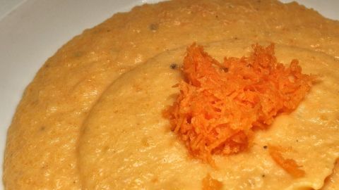 Ein cremiger Gemüsepüree mit geriebenen Karotten Toppings auf einem weißen Teller, umgeben von blühendem Porzellan.