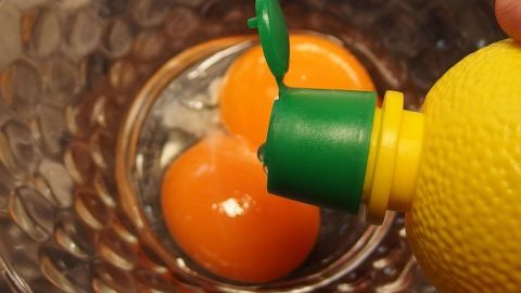 Zwei Eigelb liegen in einer Schüssel, während frischer Zitronensaft darüber gepresst wird, um Mürbeteig aufzupeppen.
