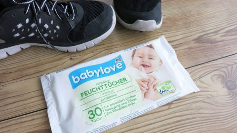 Weiße Turnschuhe stehen auf einem Holzboden neben einer Packung baby love Feuchttücher, die zum Reinigen genutzt wird.
