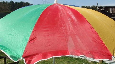 Schimmel am Sonnenschirm mit Backofenspray entfernen. Dies geht übrigens auch mit Stuhlkissen und dergleichen. Ein farbiger Sonnenschirm steht im Freien, wobei Schimmelreste auf der Oberfläche sichtbar sind.