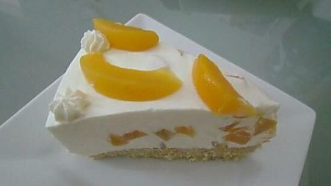 Ein Stück Joghurt-Sahne-Torte liegt auf einem Teller, garniert mit frischen Früchten und Sahnetupfen in hellem Ambiente.