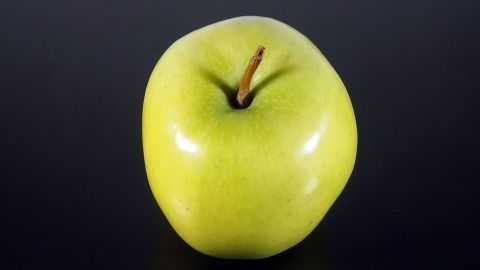 Ein grüner Apfel steht auf einem schwarzen Hintergrund, symbolisiert gesundes Essen zur Senkung des Cholesterinspiegels.