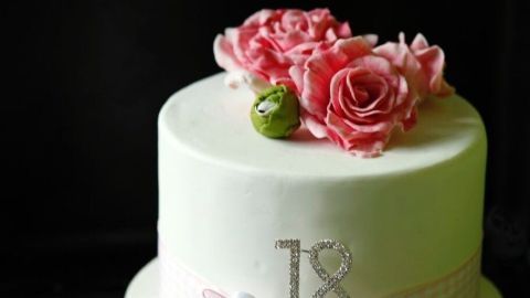 Eine elegante Zuckertorte mit einer dekorativen Schleife und Rosenblüten steht im Fokus, umgeben von dunklem Hintergrund.