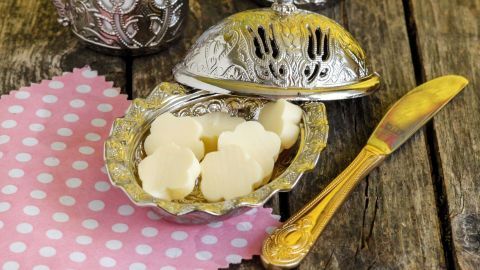 Prächtige silberne Butterdosen stehen auf einer rustikalen Holzoberfläche, während feine Butterstückchen bereitliegen.