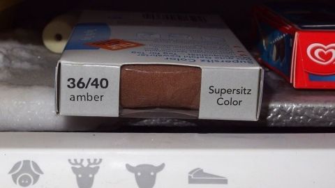 Nylonstrumhosen oder Strümpfe vor dem ersten Tragen über Nacht in der Verpackung in das Gefrierfach legen. Eine Verpackung mit Strumpfhosen in der Farbe "Amber" und der Größe "36/40" liegt auf einem Regal.