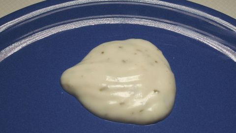 Eine cremige Knoblauchsoße liegt auf einem blauen Teller, bereit zum Servieren, in einer neutralen Küchensituation.