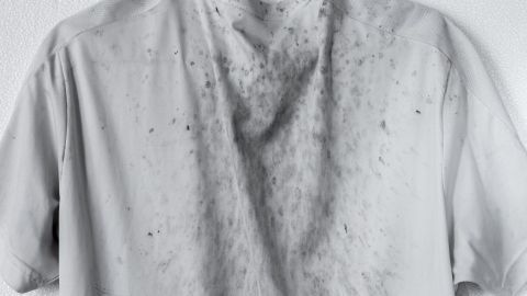 Ein verschmutztes, graues T-Shirt mit Schmier- und Ölflecken hängt an einer Wand.