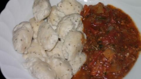 Zarte Frischkäse-Gnocchi liegen auf einem Teller neben einer würzigen Tomatensoße, bereit zum Servieren.