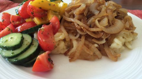 Kässpätzle liegt neben frischem, buntem Gemüse auf einem Teller, umgeben von einem rustikalen Tisch.