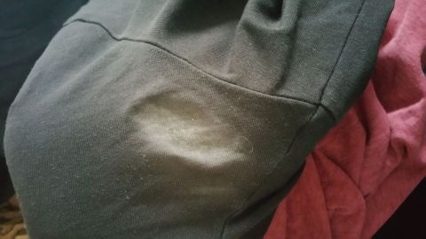 Dunkle Kleidung mit sichtbaren Schweißflecken liegt auf einem Haufen, umgeben von einem roten Kleidungsstück.