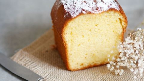 Ein Becher-Rührkuchen mit Joghurt steht auf einem rustikalen Tisch, geschnitten und bereit zum Servieren.