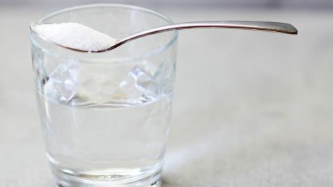 Ein Glas mit Wasser enthält einen Löffel Salz, der darauf deponiert ist, um eine Lösung für die Einweg-Nasendusche vorzubereiten.