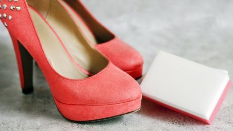 Rote Schuhe stehen neben einem Reinigungsschwamm auf einer grauen Oberfläche, bereit für die Pflege und Fleckenentfernung.