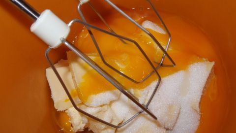 Ein Mixer mit Rührbesen steht über einer Schüssel mit Zucker und Eiern, während die Zutaten für den Mohnkuchen vorbereitet werden.