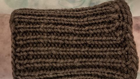 Ein gestrickter Stulpen umgibt einen Arm, während er wohlig auf einer weichen Oberfläche liegt, um kalte Hände zu wärmen.