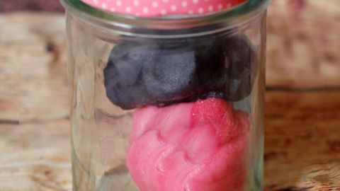 Ein Glasbehälter enthält rosa und schwarze Knetmasse, dekoriert mit einem Etikett „Homemade“ auf einem Holztisch.