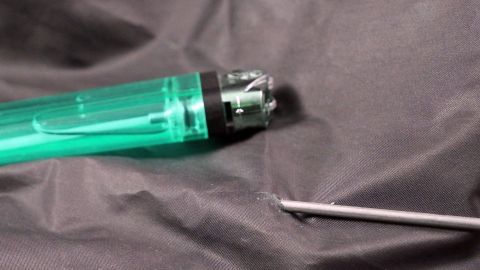 Ein grüner Stift liegt auf schwarzem Stoff und ein Metallwerkzeug ist daneben platziert, bereit zum Löcher machen in Leder.