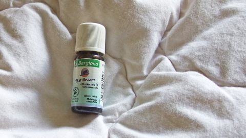 Eine Flasche Teebaumöl liegt auf einer weißen Bettdecke, um Hausstaubmilben zu bekämpfen und das Bett zu reinigen.