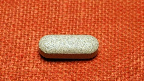 Eine Tablette liegt auf einem orangen Stoff. Sie hat eine ovaler Form und einen leicht strukturierten Hafen, was das Schlucken herausfordernd machen kann.