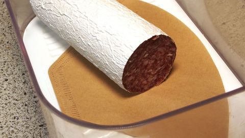 Kaffeefilter mit in die Käse- oder Wurstbox geben und damit das Ansammeln von Feuchtigkeit verhindern. In einer durchsichtigen Plastikschüssel liegt eine Salami auf einem braunen Entfeuchter, um Feuchtigkeit zu verhindern.