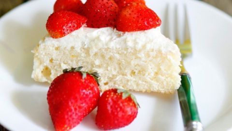 Auf einem Teller liegt ein Stück Erdbeer-Mascarpone-Kuchen, garniert mit frischen Erdbeeren, umgeben von weiteren Erdbeeren.