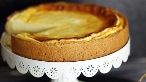 Ein Käsekuchen steht in einer eleganten Form auf einem Tisch, während ein Stück auf einem Teller geschnitten wird.