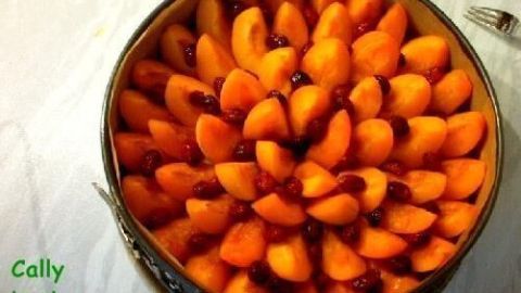 Aprikosenkuchen mit leuchtend orangefarbenen Aprikosen und roten Cranberries in einer runden Form auf weißem Tisch.