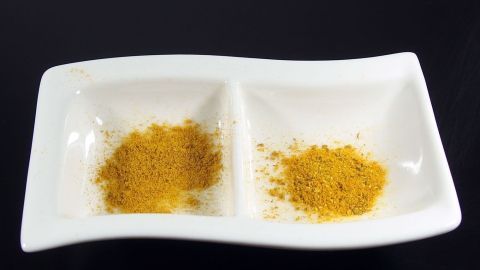 Eine weiße Schale enthält zwei Portionen von Curry-Gewürzmischung, die auf schwarzem Untergrund angeordnet sind.