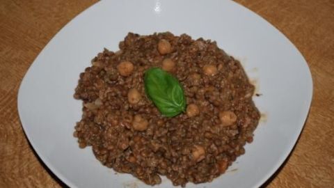 Ein weißer Teller zeigt Linsen-Chili con Carne, das gut gewürzt und mit einer grünen Pflanze garniert ist.