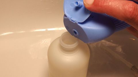 Eine Hand hält einen blauen Spender über eine weiße Flasche, um Ersatz Flüssigseife einzufüllen.