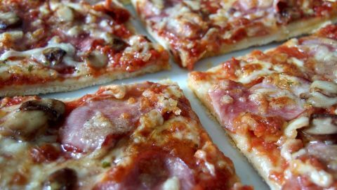 Mit einer Pizzaschere geht das Schneiden von Pizza viel leichter und sauberer von Statten! Eine Pizzaschere schneidet eine köstliche, gut belegte Pizza in gleichmäßige Stücke auf einem Teller.