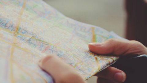 Eine Person hält einen Stadtplan in der Hand und sucht darauf nach Wegen, während sie in einer städtischen Umgebung steht.