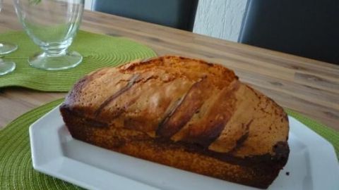 Ein Mamorkuchen liegt frisch gebacken auf einem weißen Teller. Im Hintergrund befinden sich grüne Platzdeckchen und Gläser.