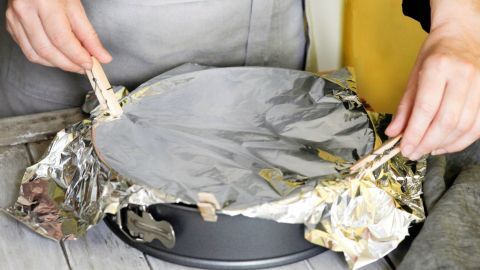 Eine Hand befestigt mit Wäscheklammern die Folie auf einer Kuchenform, um den Kuchen beim Transport zu schützen.