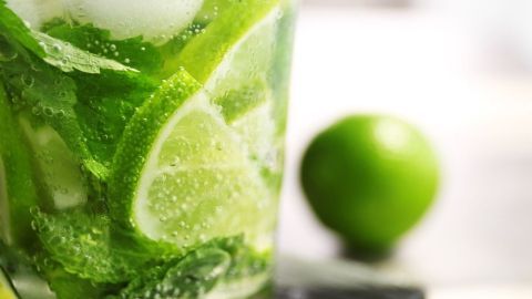 Ein Glas erfrischender Limetten-Minz Limonade mit Eiswürfeln und frischen Minzblättern steht auf einem Tisch, umgeben von einer Limette.