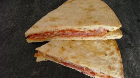 Zwei übereinander gelegte, dreieckige Fertigpizza-Stücke liegen auf einer dunklen Steinplatte, die Füllung erscheint tomatig.