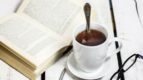 Eine Tasse schwarzer Tee steht auf einem Tisch, während ein Buch daneben aufgeklappt liegt; eine entspannte Leseatmosphäre.