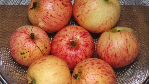 Saftige Äpfel liegen in einem Sieb, bereit zum Kochen, um das Brathähnchen zart und aromatisch zu halten.