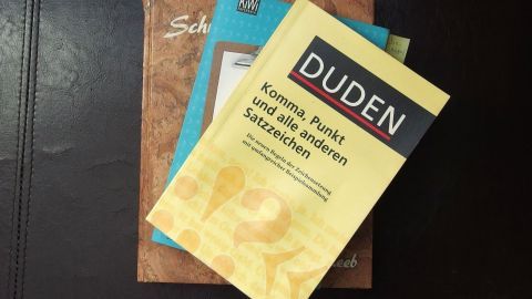 Drei Bücher liegen gestapelt. Oben ein gelber Duden mit dem Titel: "Komma, Punkt und alle anderen Satzzeichen".
